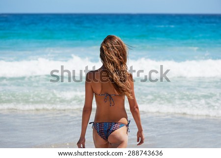 Beautiful young woman walking on the beach looking at waves shot from behind showing toned beach bum