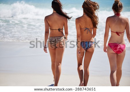 Sexy women with toned bums and beach bodies wearing colourful bikinis walk into the sea