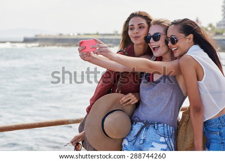 Group of teenage friends taking a happy selfie on vacation beach promenade smiling and pursing lips