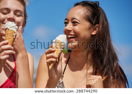 Close up portrait two women eating ice cream in the summer mixed race woman has cute smile low angle shot with blue sky background