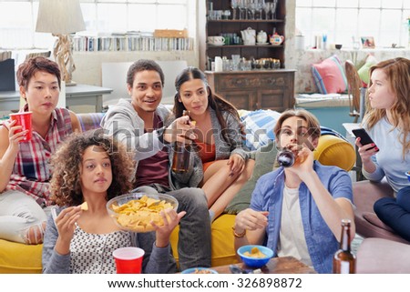 Multi ethnic group of  student friends bonding over sports match on TV drinking beer eating snacks  hanging out at home
