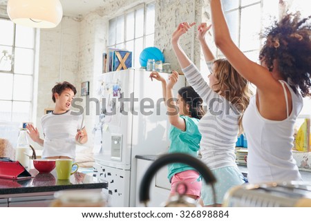 Four multi racial girl friends in kitchen at home wearing pajamas dancing wildly arms in air copying moves swinging hips