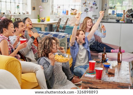 Diverse mix of friends sports fans watching winning football match on TV at home Celebrating winning goal huddled on couch shouting excited  sharing snacks drinking beer
