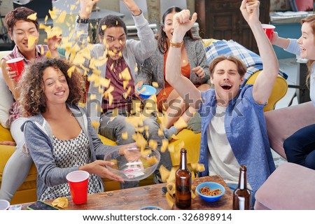 Celebrating multi racial group of sports fans student friends sharing snacks celebrating winning goal for season drinking beer throwing chips celebrating sport match