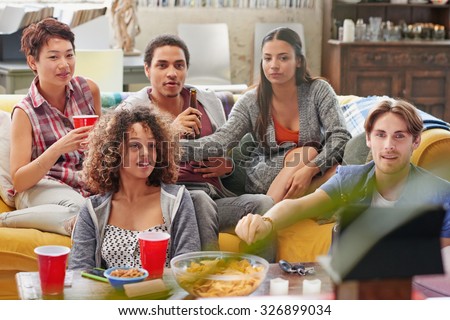 Multi ethnic group of  student friends hanging out at home huddled on couch together excitedly watching football event on TV drinking beer  eating snacks anticipating winning goal