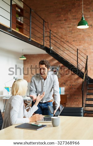 Business manager discussing work with colleague in busy office studio
