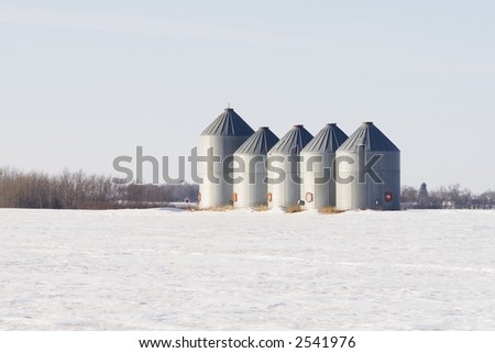 A group of grain storage bins in a winter field.