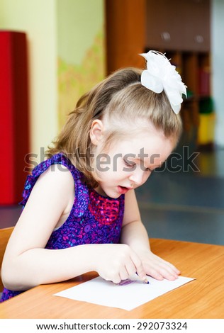The girl sitting at the table and drawing with colored pencils
