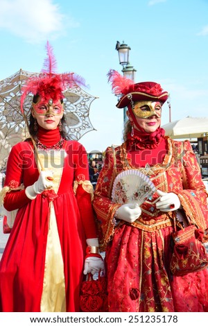 VENICE, ITALY - FEBRUARY 8: An unidentified couple of women dress red fancy dresses, white gloves and hats with red feather during Venice Carnival at Piazza San Marco on February 8, 2015 in Venice.