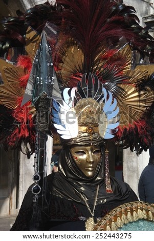 VENICE,ITALY-FEBRUARY 8:An unidentified man dresses black fancy dresses with gold masks, red and black feather hat and carries a spear during Carnival at Piazza San Marco on February 8, 2015 in Venice