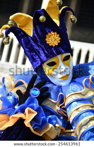 VENICE,ITALY FEBRUARY 8:An unidentified man in blue fancy dress with white mask, joker hat with rattles, big blue ring and back gloves during Carnival at Piazza San Marco on February 8, 2015 in Venice