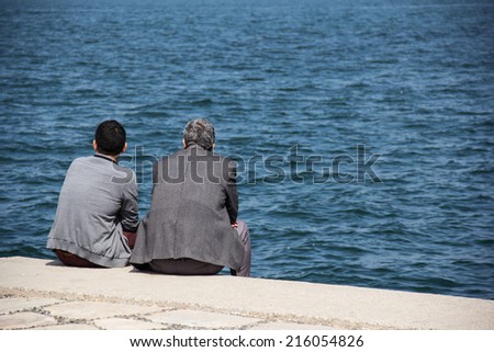 IZMIR, TURKEY - APRIL 25, 2014: Two men sit and talk together along the Izmir bay. Turkey, Izmir. APRIL 25, 2014