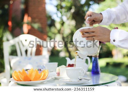 Afternoon tea with a man pouring tea from pot in to a cup