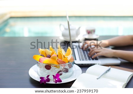 Business people working at home on laptop computer with blows of fresh fruit by swimming pool