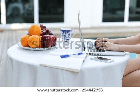 Business people working on laptop computer with plate of fresh fruit by swimming pool