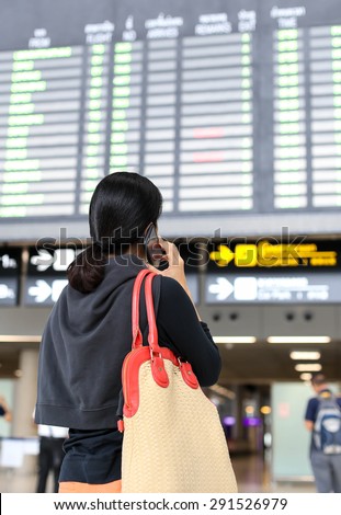 Woman on the phone and looking at flight information board in the airport