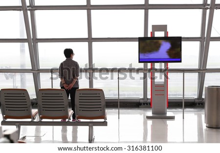 Focus on the chair back view of woman standing near the window of international airport terminal.