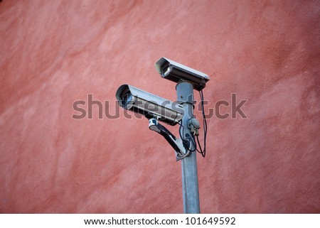 A pair of security cameras on a red wall