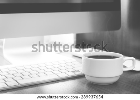 Cup of coffee and PC on wooden desk black and white color