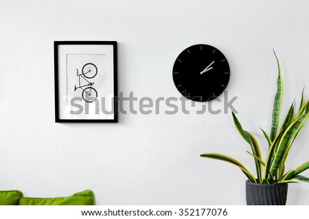 White wall decoration with a picture frame, clock and plants