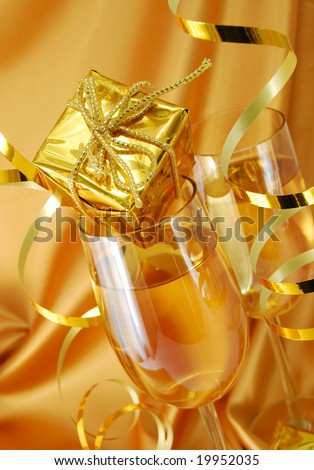 Two glasses with champagne and gift on gold background