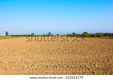 Plowed field. Arable landscape, cultivated field with bare red soil under a blue sky