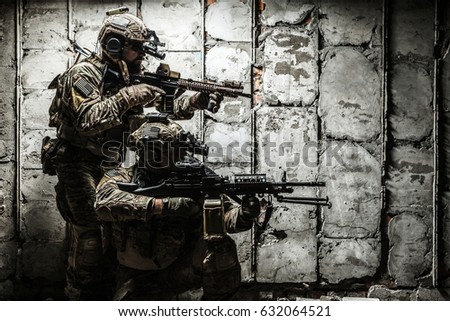 Pair of Army Rangers with rifle and machine gun moving along the concrete wall on mission. They are ready to start firing if enemy appear. Outdoor location shot