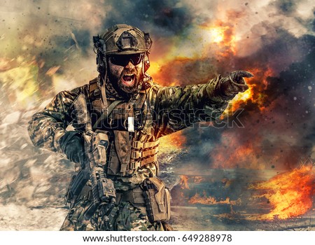 Bearded soldier of special forces in action pointing target and giving attack direction. Burnt ruins, Heavy explosions, gunfire and smoke billowing on background