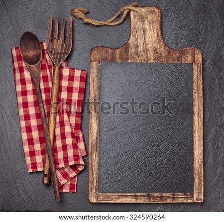 Cutting board, tablecloth, wooden spoons and piece of chalk. Over dark slate board.