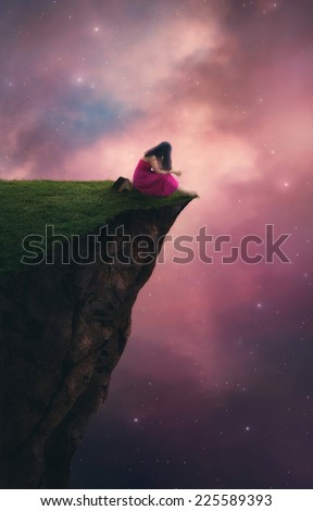 A woman praying on top of a cliff before the night sky.