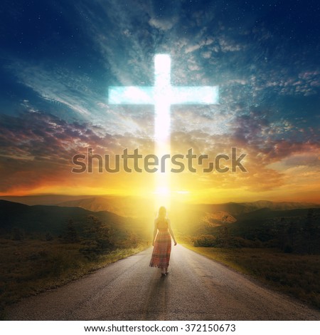 A woman walks down a road to a beautiful glowing cross.