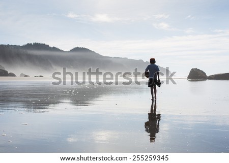 Boy Walking Away on Beach Holding a Football and Sandals