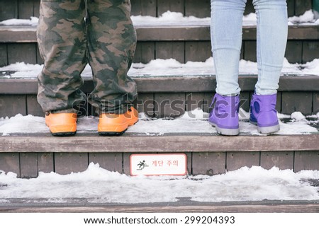 People wearing orange and purple boots to walk together . There is snow on the stairs