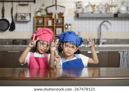 Two little chef show victory sign in the kitchen