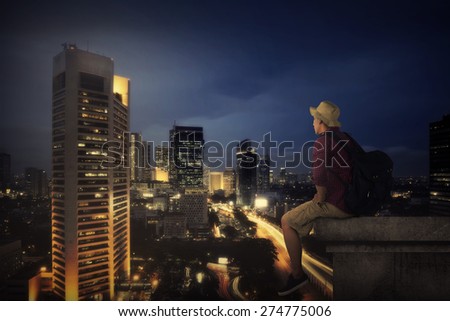 Traveler man sitting on the top of building looking at the city at night. Business travel concept