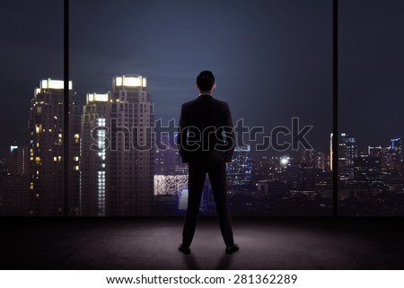 Man standing in his office looking at the city at night. Business success concept