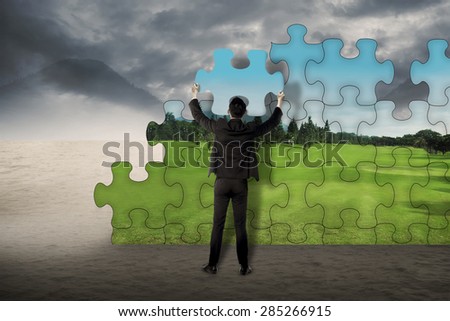 Business man holding puzzle to assembly change situation from desert to beautiful landscape