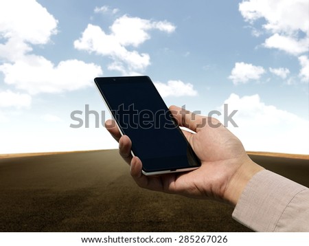 Hand holding cellphone with blank screen on empty road background. You can put your design on the cellphone