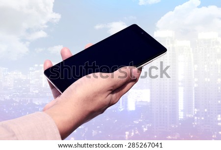 Hand holding cellphone with blank screen on cityscape background. You can put your design on the cellphone