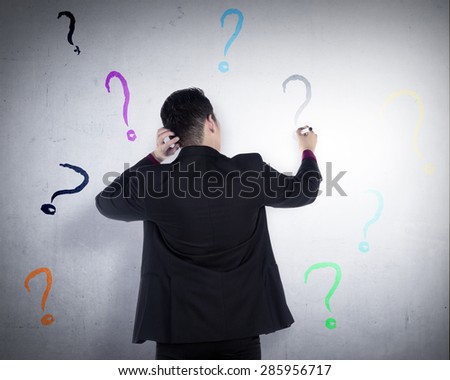 Business man write question mark on the wall. He dont know what to write