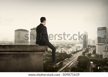 Business man sitting on building rooftop. Suicide concept image