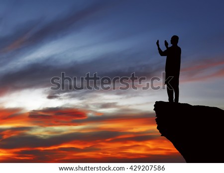 Silhouette of muslim man standing on the top of cliff. Praying and looking to the sky