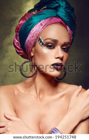 Fashion portrait of the beautiful sexy model with tanned skin in arabic ethnic accessories and colorful make-up and silk headband