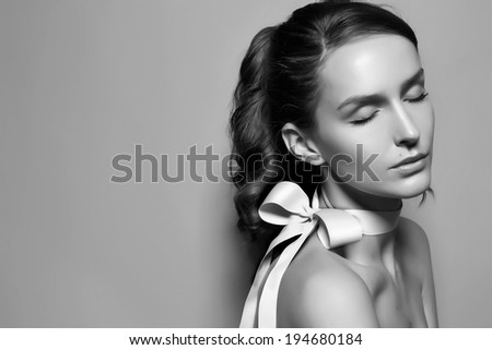 Black and white tender fashion portrait of Beautiful gentle young brunette woman with close soft eyes and sensitive mouth wearing silk bow on the neck and right shoulder