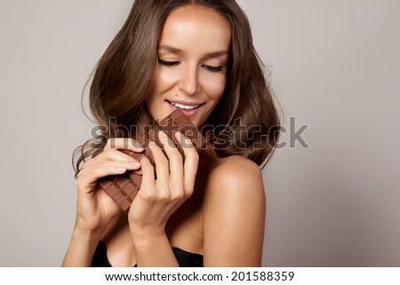 Portrait of a young beautiful girl with dark curly hair, bare shoulders and neck, holding a chocolate bar to enjoy the taste and are dieting, healthy eating and organic foods, feeling temptation