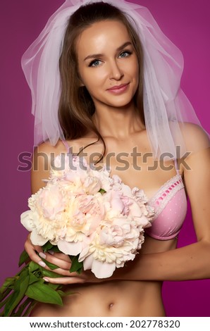Beautiful young sexy bride with long dark hair in a white veil, pink lace lingerie with bouquet of pale pink peonies with a gentle makeup