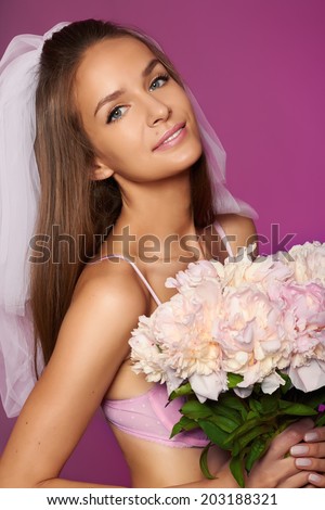Beautiful young sexy bride in white veil and pale pink lace lingerie with bouquet of peonies in hand