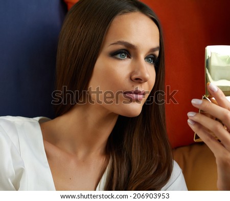 Beautiful young sexy girl with long straight hair and evening make-up, dark painted eyes and pink lipstick looks in gold powder-cases, her well-groomed skin, healthy complexion, powder oneself