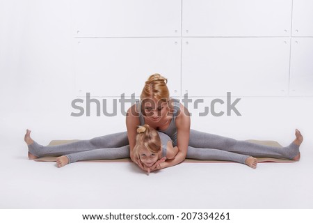 Mother daughter doing yoga exercise, fitness, gym wearing the same comfortable tracksuits, family sports paired woman child sitting on the floor stretching his legs apart in different directions pose