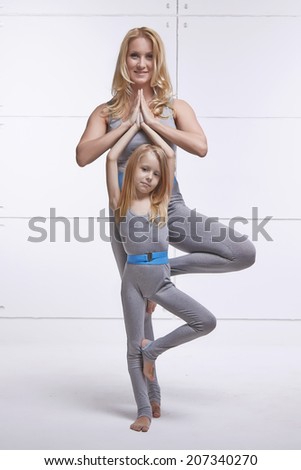 Mother and daughter doing yoga exercise, fitness, gym wearing the same comfortable tracksuits, family sports, sports paired holding one leg up
